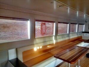 Empty train car interior with long wooden benches along windows and closed blinds.