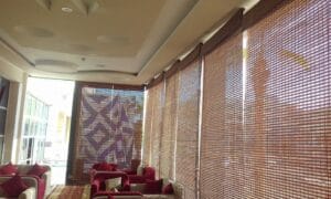 Cozy lounge with magenta cushions and white seating along a wall of woven bamboo blinds. A geometric patterned panel is visible at the end of the room.
