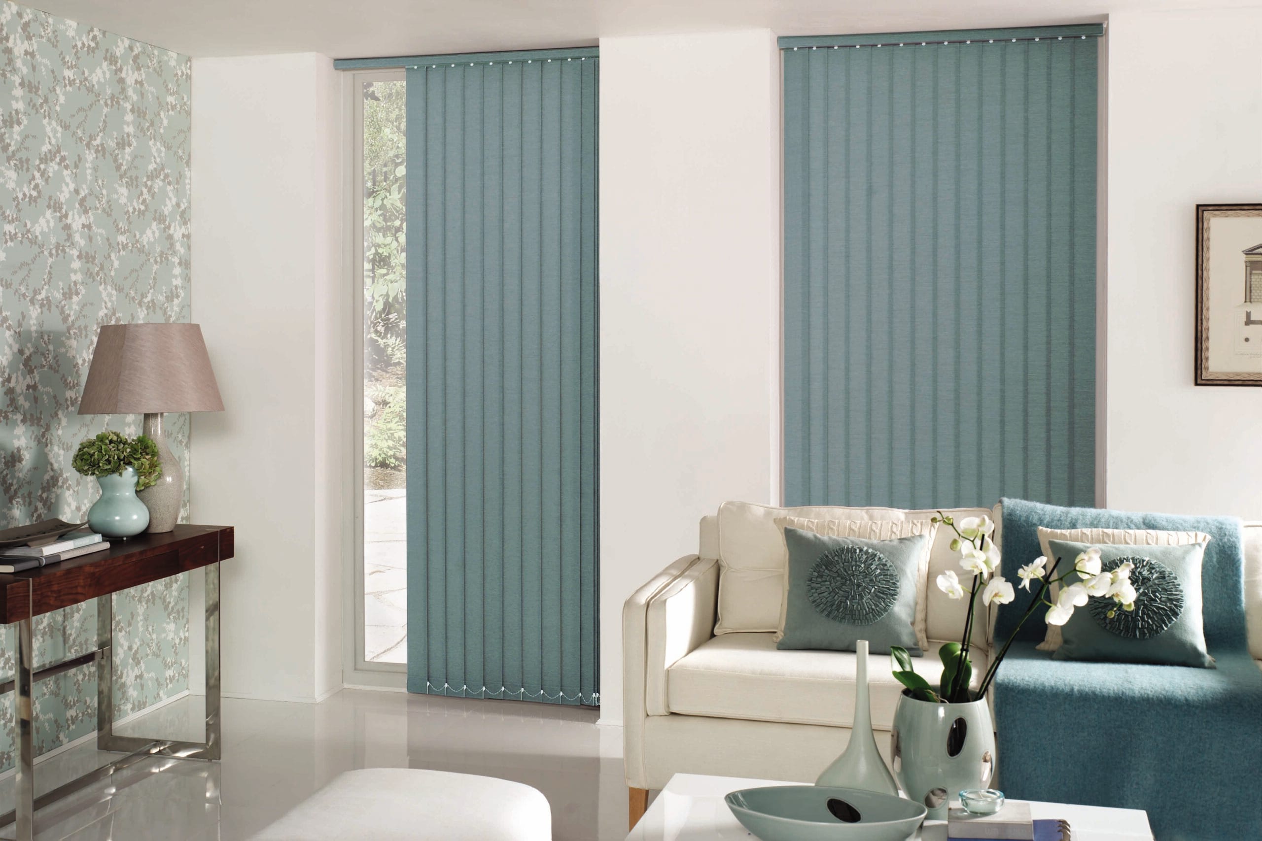 Living room interior with teal vertical blinds over windows, white walls, and a cream sofa with teal cushions.