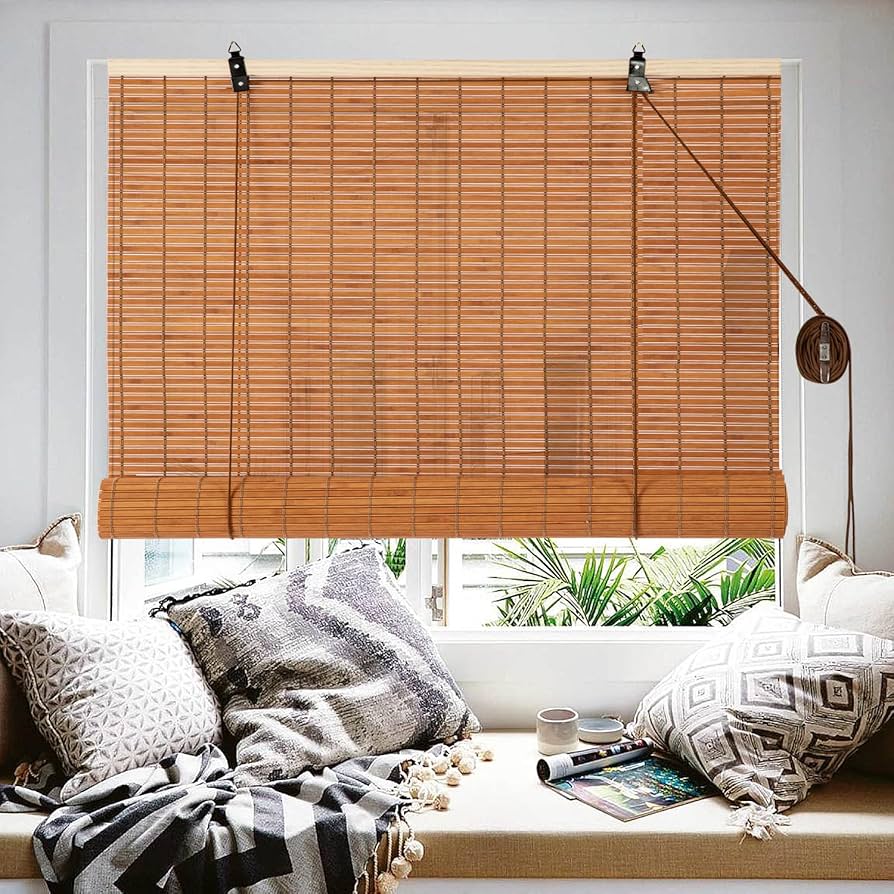 Window with a light brown bamboo blind and cord, above a cushioned window seat with patterned pillows and a throw blanket.