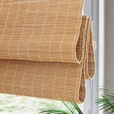Natural bamboo roll-up blinds partially lowered over a window, with greenery visible outside.