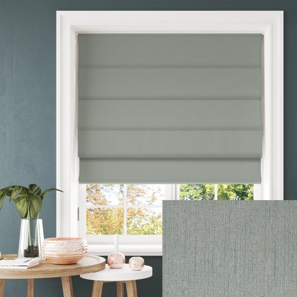 Window with gray pleated shades framed by white trim on a teal wall; a round wooden table with a pink ceramic bowl and a plant nearby.