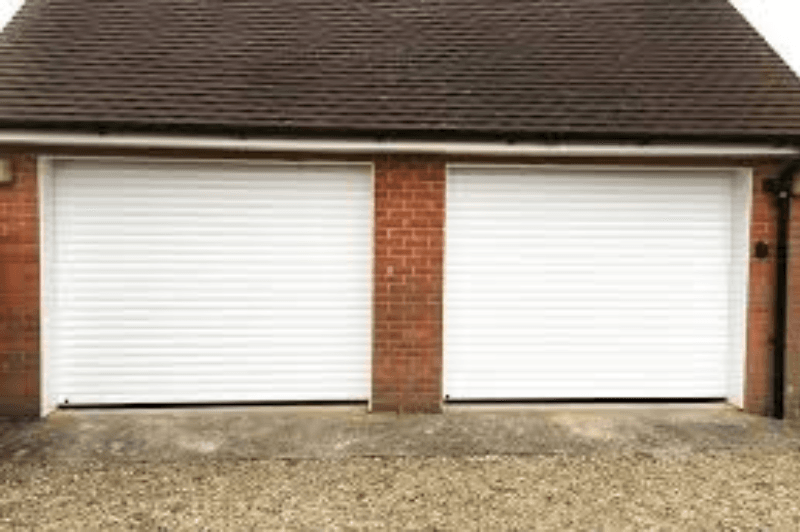 Two white garage doors side by side with a brick pillar between them on a gravel driveway.